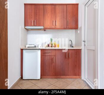 Vista frontale dell'armadio a modulo cucina in legno con piccolo frigorifero e vassoio di frutta, monolocale bianco interno in stile classico con pelliccia di quercia naturale Foto Stock