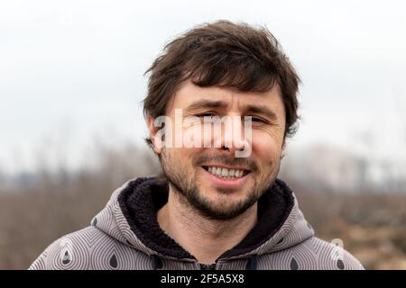 Un bell'uomo sorrideva felice fuori su uno sfondo sfocato. Uomo in giacca con cappuccio Foto Stock