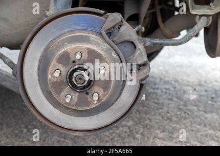 Mozzo ruota posteriore arrugginito con disco del freno presso il negozio di pneumatici. Vettura senza ruota durante la sostituzione presso il centro di assistenza pneumatici. Vista in primo piano Foto Stock