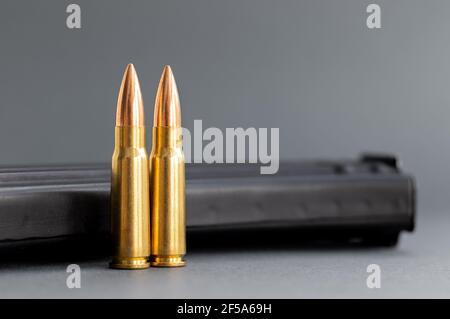 Due proiettili contro il fucile d'assalto Kalashnikov clip, rivista su sfondo grigio sfocato. Cartucce calibro 7.62 per ak 47, primo piano, fuoco selettivo Foto Stock