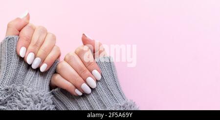 Mani femminili in pullover grigio lavorato a maglia con bella manicure - chiodi di avorio bianco su sfondo di carta rosa, banner modello con spazio per la copia Foto Stock