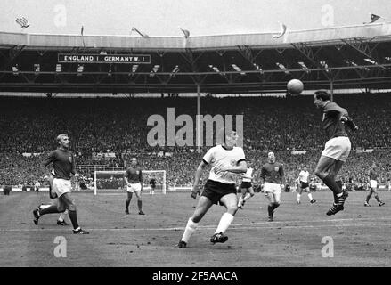 Inghilterra contro Germania occidentale finale della Coppa del mondo 1966, Wembley Stadium 20 minuti del primo tempo. Ray Wilson of England dirige la palla al Capitano Bobby Moore passando Lothar Emmerich della Germania Ovest Foto di Tony Henshaw Archive Foto Stock