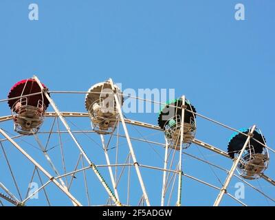 Frammento di ruota panoramica con cabine multicolore contro un cielo blu chiaro. Foto Stock