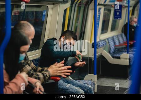 Giovane uomo che sanitizza le mani mentre viaggia con la metropolitana a Londra, Inghilterra Foto Stock