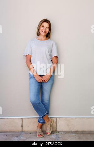 Ritratto a tutta lunghezza di una donna anziana sorridente appoggiata al muro Foto Stock