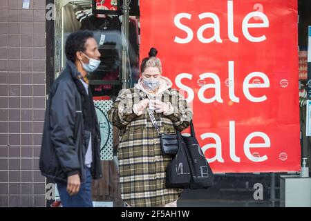 Londra, UK - 5 Febbraio, 2021 - pedoni con maschere facciali protettive e cartelli di vendita esposti in un negozio in Wood Green High Street Foto Stock
