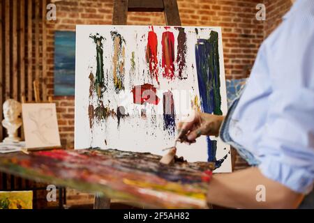 Pittore dello studio che crea un quadro astratto su tela utilizzando dipinti ad olio e coltello a palette. Giovane artista femminile che lavora. Processo creativo, relax Foto Stock