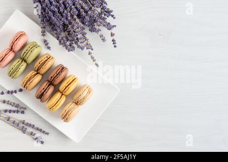 Macaroni francesi multicolore in una vista dall'alto su sfondo di legno bianco. Macaron di biscotti alla meringa francese con gusti diversi. Foto Stock