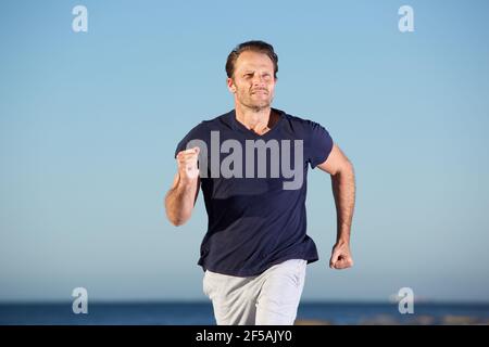 Ritratto di uomo fitness che corre all'aperto in riva al mare Foto Stock