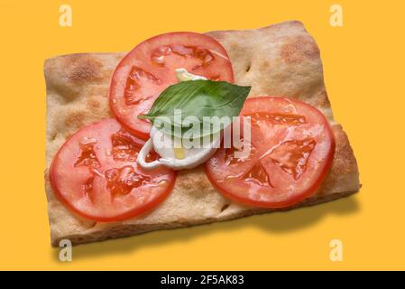 Fetta di focaccia ligure con pomodoro fresco, mozzarella, foglia di basilico e olio extravergine d'oliva - isolata in giallo, vista dall'alto Foto Stock