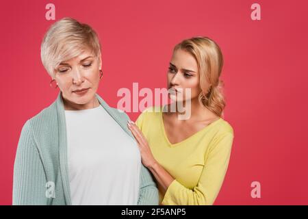 donna preoccupata che tocca la madre offesa isolata sul rosa Foto Stock