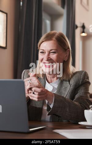 Donna d'affari matura seduto al tavolo in caffetteria e. parlare online con il suo collega utilizzando un computer portatile Foto Stock