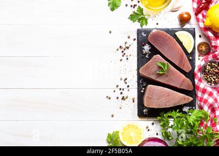 Bistecche fresche di tonno crudo su piastra di ardesia nera su sfondo bianco. Vista dall'alto con copyspace. Foto Stock