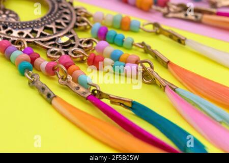 Decorazioni etniche su fogli colorati di paper.Women's Jewelry con una base metallica rotonda, con perle e piume colorate Orecchini anelli Amulets. Giallo Foto Stock