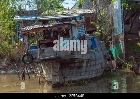 La vecchia barca da pesca si trova sulle rive del Mekong. Sullo sfondo, case in ferro ondulato Foto Stock