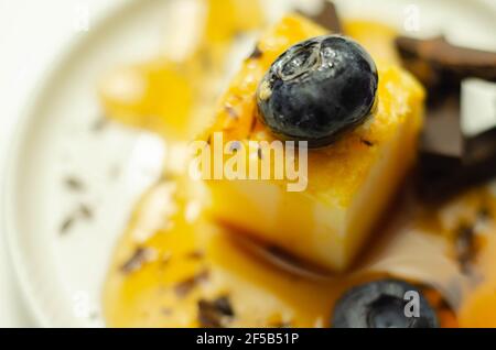 Una porzione di cheesecake alla vaniglia decorata con mirtilli e pezzi di cioccolato al latte, condita con salsa al caramello, dolce pausa Foto Stock