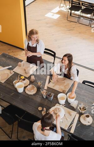 Vasai femmina durante il processo di lavorazione nell'officina di argilla. Maestri di donna preparano prodotti in ceramica e argilla a grande tavolo di legno. Foto Stock