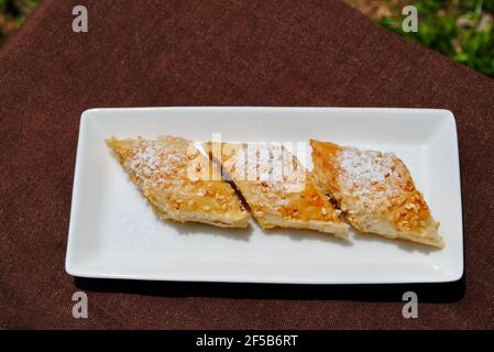 Baklava fatta in casa su piatto rettangolare bianco su tovaglia marrone.dolci casalinghi cotti con sesamo sulla parte superiore. Foto Stock