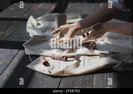 Mani macchiate in argilla andando prendere utensile tagliato da tavola di legno, concetto di arte terapia. Foto Stock