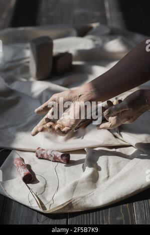 Mani macchiate in argilla andando prendere utensile tagliato da tavola di legno, concetto di arte terapia. Foto Stock