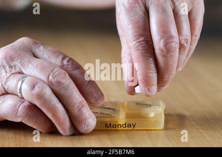 Closeup di una donna anziana le mani di una donna anziana che prende il suo farmaco per la settimana in una scatola di pillola su tavola di legno, business, concetto di salute Foto Stock