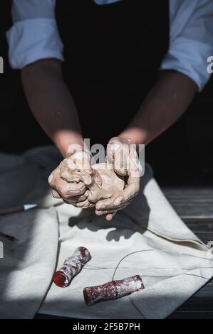 Mani bagnate ricoperte di argilla grigia di vasaio che tiene pezzo grezzo di argilla. Foto Stock