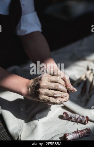 Mani bagnate ricoperte di argilla grigia di vasaio che tiene pezzo grezzo di argilla. Foto Stock