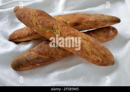 Una pila di baguette fatte in casa appena sfornate su un crumpled tovaglia damask bianca Foto Stock