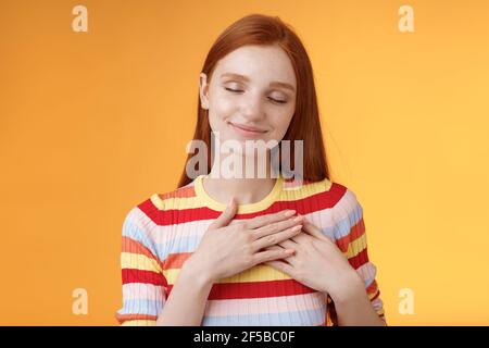 Il cuore mantiene caldi i ricordi più cari all'interno. Sorridente tenero heartwarming rosso testa bella ragazza toccare petto grinning occhi chiusi ricordare bello bello Foto Stock