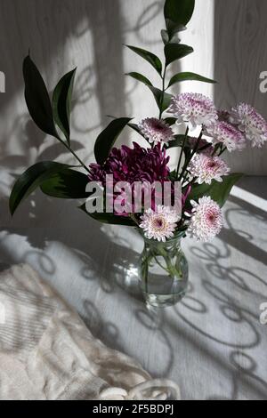 Bel bouquet di dahlias viola e bianco in vaso di cristallo su sfondo grigio legno. Foto Stock