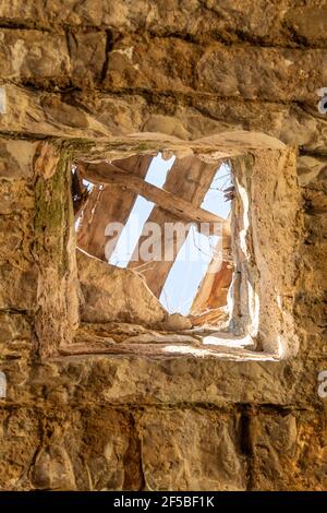 buco in vecchio muro di pietra attraverso il quale si può vedere il cielo blu Foto Stock