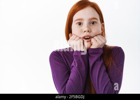 Affascinato bambina rossa guardare con interesse e stupore, guardare qualcosa di mozzafiato e impressionante, in piedi stupito contro il bianco Foto Stock