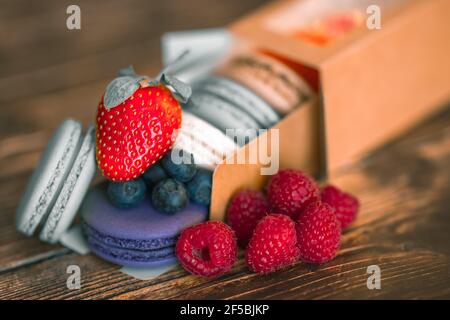 Bacche fresche di mirtilli, lamponi e fragole, accanto ai biscotti macaroon Foto Stock