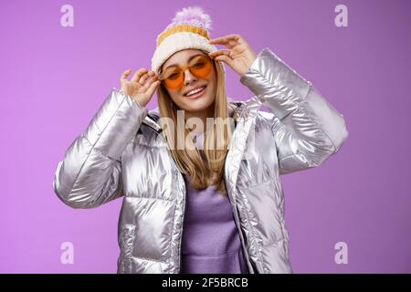 Elegante sassy audace bionda europea ragazza che agisce fresco indossare elegante occhiali da sole giacca argento cappello invernale controllo cornici naso testa inclinabile sorridente allegro Foto Stock