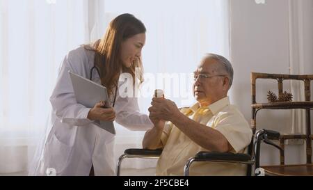 Il medico della giovane donna asiatica prescrive la medicina al paziente anziano disabile sulla sedia a rotelle quando il tempo del paziente anziano dell'uomo anziano a Vai a casa. Medicina e h Foto Stock