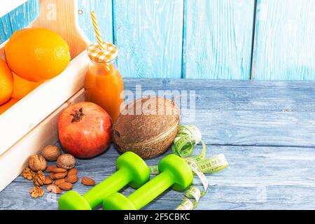 Una bottiglia di succo, frutta e noci, un nastro di misurazione su uno sfondo testurizzato in legno. Fitness, nutrizione sportiva Foto Stock