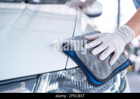 La mano dell'uomo tiene la microfibra in mano e lucida l'automobile, concetto di servizio di lavaggio dell'automobile. Foto Stock