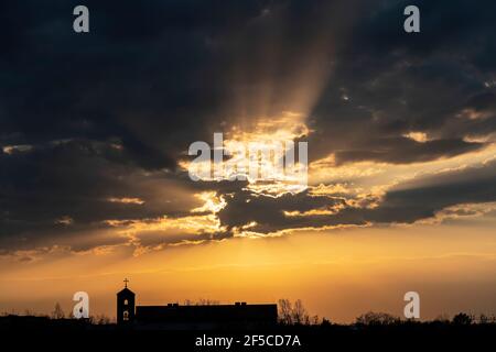 Spettacolare tramonto arancione come fuoco nel cielo con nuvole scure. Raggi di luce che brillano attraverso nuvole scure. Foto Stock