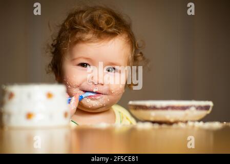 Il bambino piccolo carino sta alimentando usando il cucchiaio. Bambino piccolo che mangia purea di frutta all'interno. Foto Stock