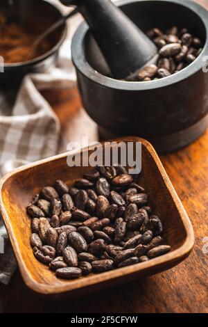 Fagioli di cacao arrostiti in ciotola su tavola di legno. Foto Stock