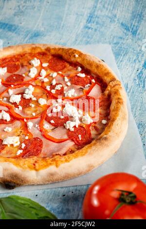 Pizza croccante con salame, prosciutto, pepe e formaggio casereccia. La pizza giace su uno sfondo blu. Foto Stock