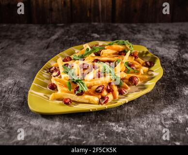 Abbondante pranzo di patatine fritte, salsicce e rucola. Piatto in un piatto giallo su un tavolo di cemento grigio. Il concetto di cibo nutriente. Foto Stock