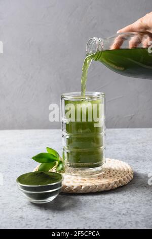 Versare una bevanda di Chlorella sana Detox in vetro da bottiglia su un tavolo grigio. Foto Stock