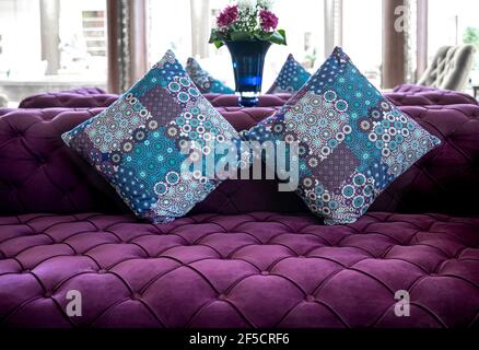 Moderno divano in tessuto di velluto viola con bottoni incassati e cuscini decorativi colorati. Idea e variante di tessuto per divani da tappezzeria. Foto Stock