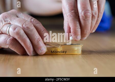 Closeup di una donna anziana le mani di una donna anziana che prende il suo farmaco per la settimana in una scatola di pillola su tavola di legno, business, concetto di salute Foto Stock