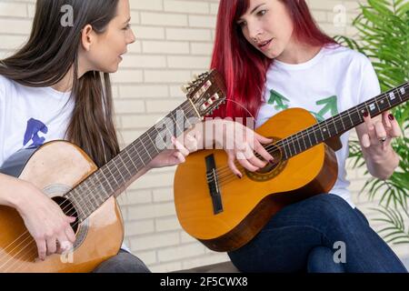 Giovani donne in t-shirt con simbolo transgender che gioca chitarre e parlando contro muro di mattoni Foto Stock