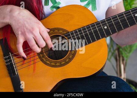 Ritagliare la femmina nella t-shirt con il simbolo transgender che tocca le corde di chitarra acustica durante la riproduzione della canzone Foto Stock