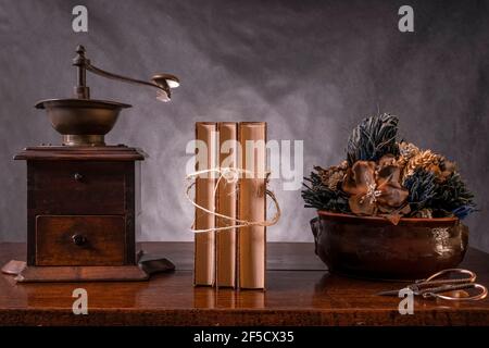 Un macinacaffè antico, un vaso di fiori secchi e tre vecchi libri legati con corda su un tavolo di legno Foto Stock