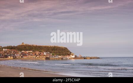 Vista panoramica di una città sul mare. Gli edifici della città sono illuminati da un sole sbiadente e le rovine di un castello si trovano sulla cima di una collina. Foto Stock