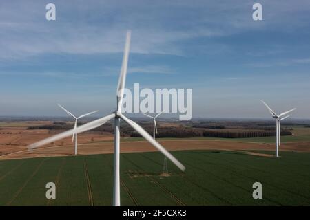 Vista aerea di un parco eolico su terreni agricoli verdi con grandi turbine bianche che generano energia rinnovabile verde durante una crisi energetica Foto Stock